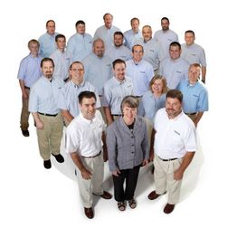 Group of 21 people in business casual attire, standing together and smiling at the camera.