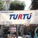 Striscione di promozione per "Turtù", negozio di bici e scooter, su una strada alberata.