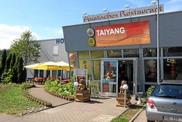 Asiatisches Restaurant mit Terrasse und gelben Sonnenschirmen, Auto im Vordergrund.