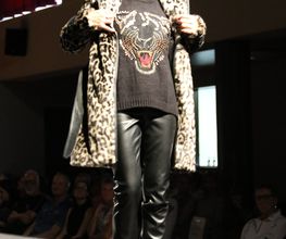 Eine Person auf dem Laufsteg mit Leopardenmantel, schwarz bedrucktem Pullover und Sonnenbrille.