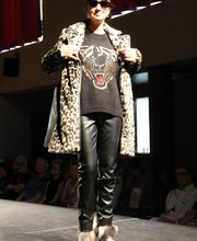 Eine Person auf dem Laufsteg mit Leopardenmantel, schwarz bedrucktem Pullover und Sonnenbrille.