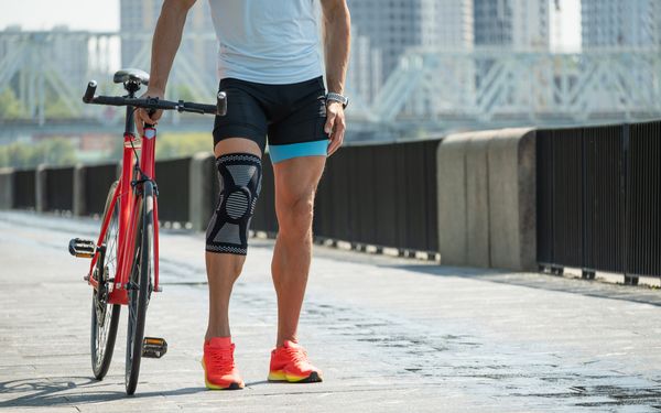 Mann schiebt sein Fahrrad. Um sein Knie hat er eine Orthese angelegt.