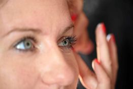Nahaufnahme eines Frauenauges mit langem Wimpern und bemalten Fingernägeln im Hintergrund.