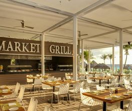 Restaurante al aire libre "Market Grill" con mesas, sillas blancas y vista al mar.