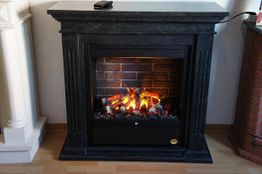Kamin mit schwarzem Rahmen, brennende Holzscheite und Flammen aus Kunstlicht auf Holzboden.