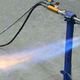 Bruciatore a gas acceso su un supporto blu con fiamma blu e arancione su sfondo grigio.