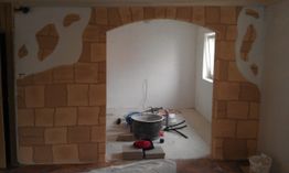 Baustelle mit bemalter Wand als Steinbogen, Werkzeuge und Eimer auf dem Boden im weißen Raum.