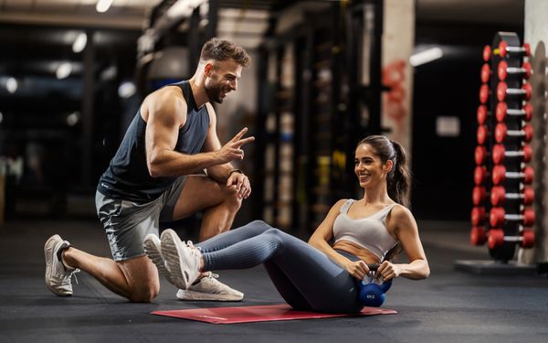 Personal Fitnesstrainer zählt einer Übung für seine Trainingspartnerin runter. Die beiden befinden sich in einem Fitnessstudio.