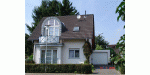 Zweistöckiges Einfamilienhaus mit Giebelfenster und Garage, umgeben von Bäumen.