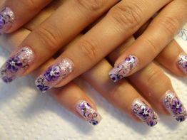 Lila Blumen-Nailart auf langen, glitzernden Nägeln. Hände auf weißem Hintergrund.
