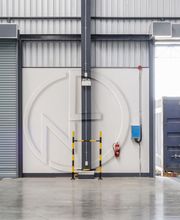 Magazzino con carrello elevatore bianco fermo vicino a portone aperto e container blu.