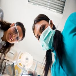Two dental professionals wearing masks and goggles, seen from a patient's perspective.