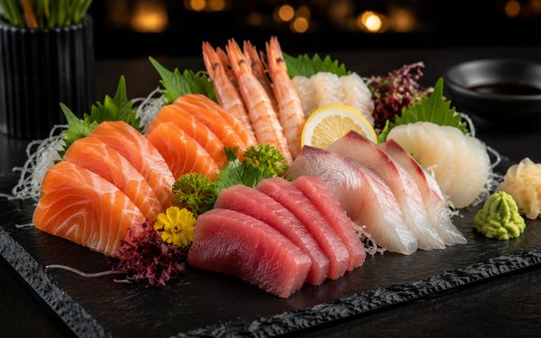 Verschiedene Arten Fisch als Sashimi angeordnet auf einer Schieferplatt.