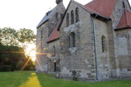 Alte Kirche mit Steinwänden bei Sonnenuntergang, Sonne strahlt durch die Bäume im Hintergrund.