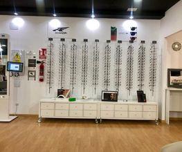 Tienda de óptica con expositores de gafas vacíos y muebles blancos sobre piso de madera.