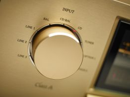 Goldener Audioverstärker-Drehknopf mit Ein- und Ausgangsoptionen für verschiedene Quellen.