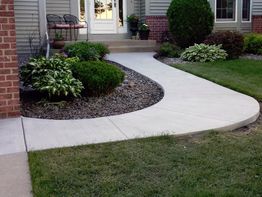 Curved concrete path with plants leading to a porch of a house.