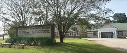 Exterior of Dale County Government Building with a large sign and trees in front.