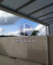 Varanda com cobertura de vidro, céu azul e nuvens ao fundo.