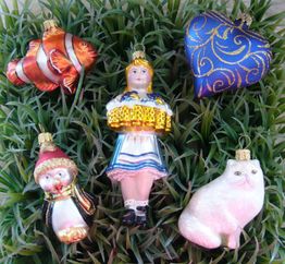 Fünf bunte Weihnachtsanhänger: Fisch, Herz, Pinguin, Mädchen und Katze, platziert auf grünem Gras.