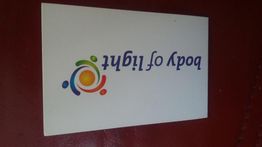 Witte kaart met gekleurd logo en tekst "body of light" op een rood oppervlak, ondersteboven.