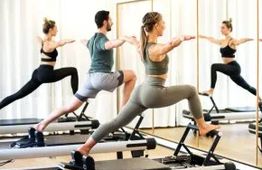 People doing Pilates on reformers in a studio, performing a warrior pose.