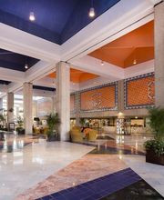 Vestíbulo de hotel amplio y colorido, con techos altos y plantas decorativas.