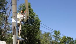 Worker on elevated platform fixing power lines against a clear blue sky.