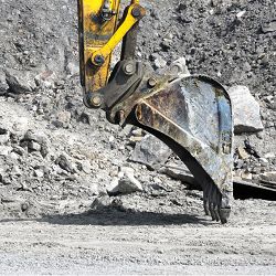 Excavator bucket digging into rocky ground.