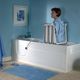 Vrouw in een badlift in een blauw betegelde badkamer, zittend naast een witte badkuip.