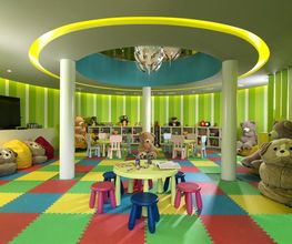 Sala de juegos infantil colorida con alfombra de rompecabezas, peluches y mesas pequeñas.