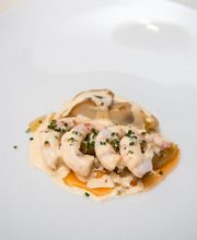 Plato gourmet con marisco en salsa sobre un plato blanco.