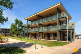 Three-story apartment building with green railings and outdoor stairs under a clear blue sky.
