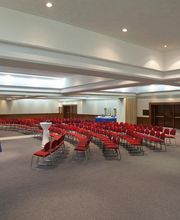 Sala de conferencias vacía con filas de sillas rojas y un podio a la izquierda.