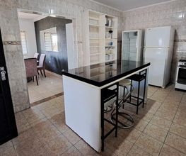 Cozinha com ilha central, cadeiras, geladeira, fogão e acesso à sala de jantar ao fundo.