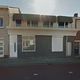 Rij van huizen met etalageramen en gesloten luiken onder blauwe lucht.
