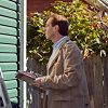 Person inspecting a house exterior with a clipboard, next to a green wall and garden.