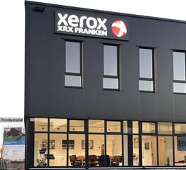 Gebäude mit Xerox XRX Franken Logo, große Fenster, modernes Design, Himmel im Hintergrund.