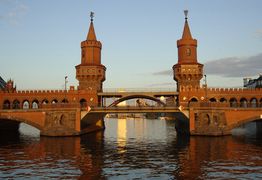 Backsteinbrücke mit zwei Türmen über einem Fluss, beleuchtet vom sanften Licht der Abendsonne.