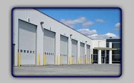 Industrial building with several large garage doors, set against a partly cloudy sky.