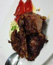 Plato de carne asada con guarnición de pimientos rojos y salsa en un plato blanco.