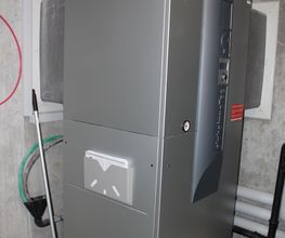 Silberne Heizungsanlage in einem Keller mit Besen und Rohren neben der Wand.
