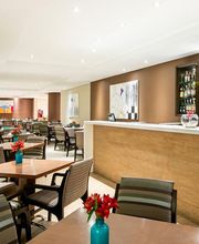 Restaurante moderno com mesas, cadeiras e um balcão de bar, decoração com flores vermelhas.