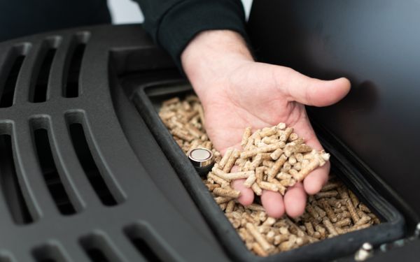 Ein Mann hält das Granulat über seinen modernen schwarzen Pelletofen in der Hand.