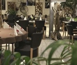 Gemütliches Restaurant mit Holzdekor, gedeckten Tischen und grüner Pflanze im Vordergrund.