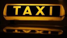 Gelbes Taxi-Schild mit schwarzer "TAXI"-Aufschrift, nachts beleuchtet.