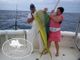 Two people holding a large fish on a boat, with ocean in the background.