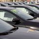 Row of black cars for sale, with price tags on windshields, parked in a dealership lot.