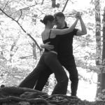 Paar tanzt Tango im Freien, schwarz-weiß, mit Bäumen im Hintergrund.