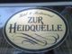 Ovales Schild mit der Aufschrift "Hotel & Restaurant Zur Heidquelle" in eleganter Schriftart.